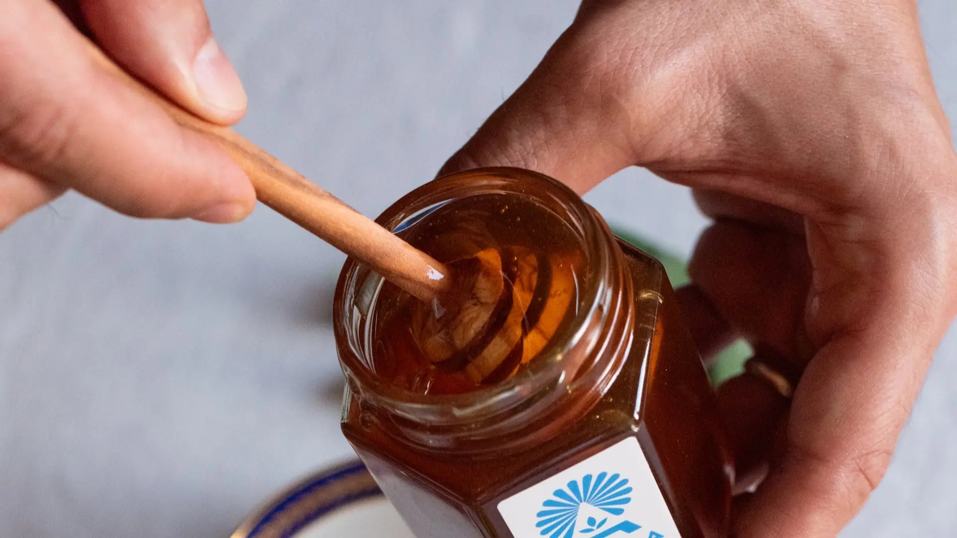 Scooping Greek thyme honey from a glass Arma Honey branded jar