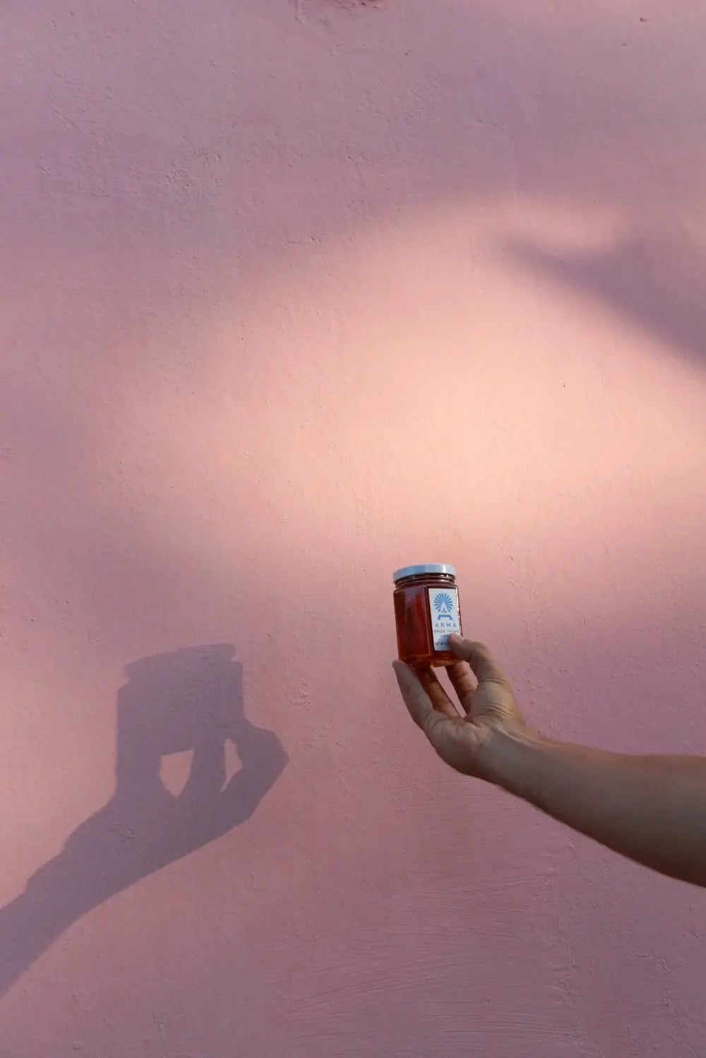 Hand holding a jar of Arma Greek Thyme honey against a pink wall with a soft focus effect