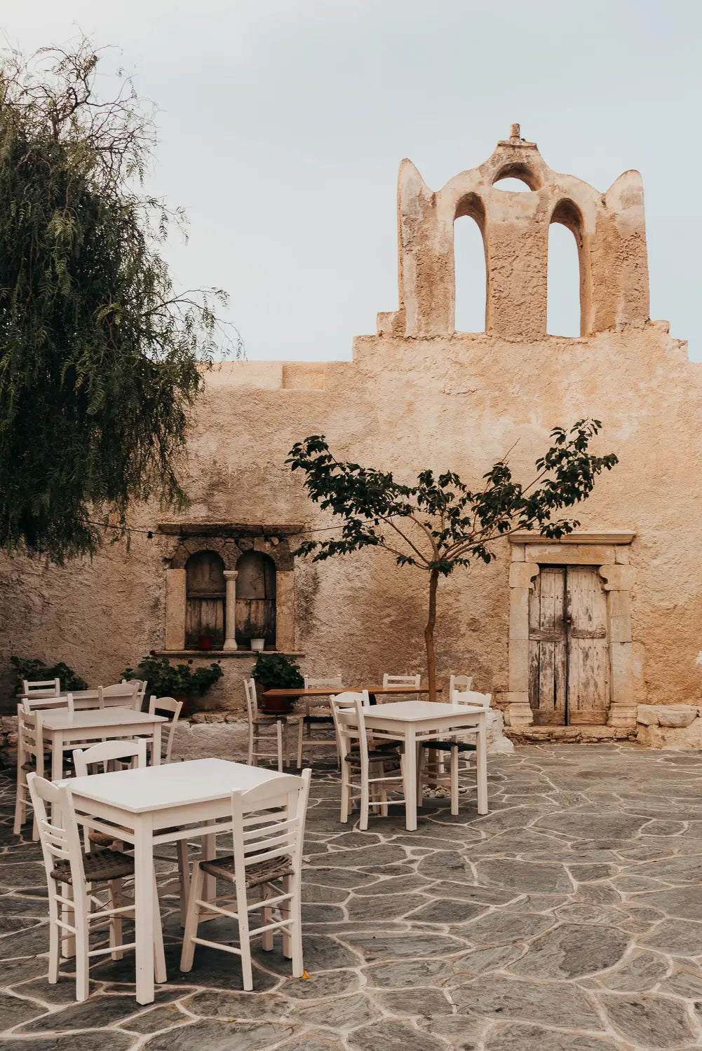 Outdoor seating area with tables and chairs in front of a rustic building with bell towers.